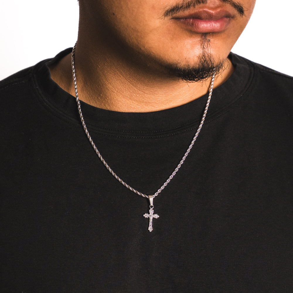 Man wearing a black shirt with a silver chain necklace featuring a cross pendant.