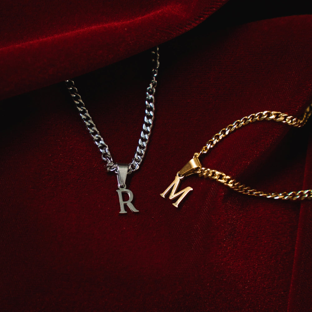 Two necklaces with 'R' and 'M' pendants on a red velvet background