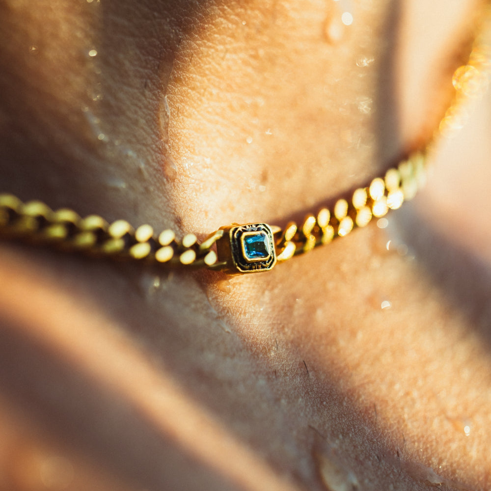 Gold bracelet with a blue gemstone on a person's wrist