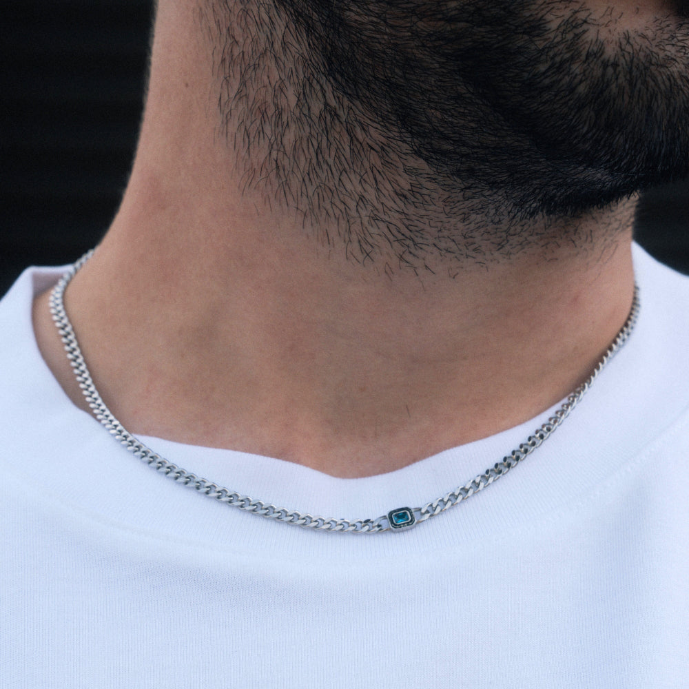 Close-up of a person wearing a silver chain necklace with a blue gemstone on a white background