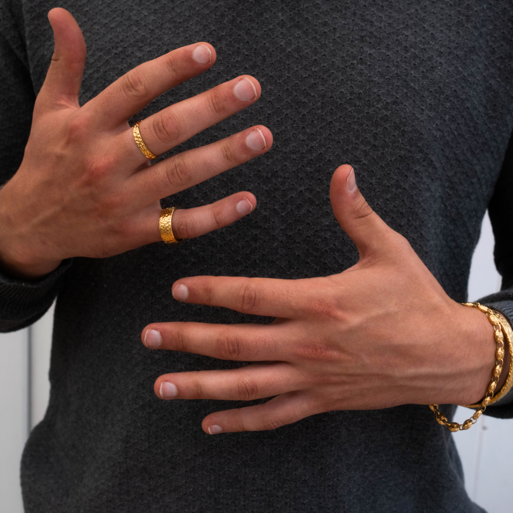Close-up of hands wearing gold rings and bracelets on a dark textured background
