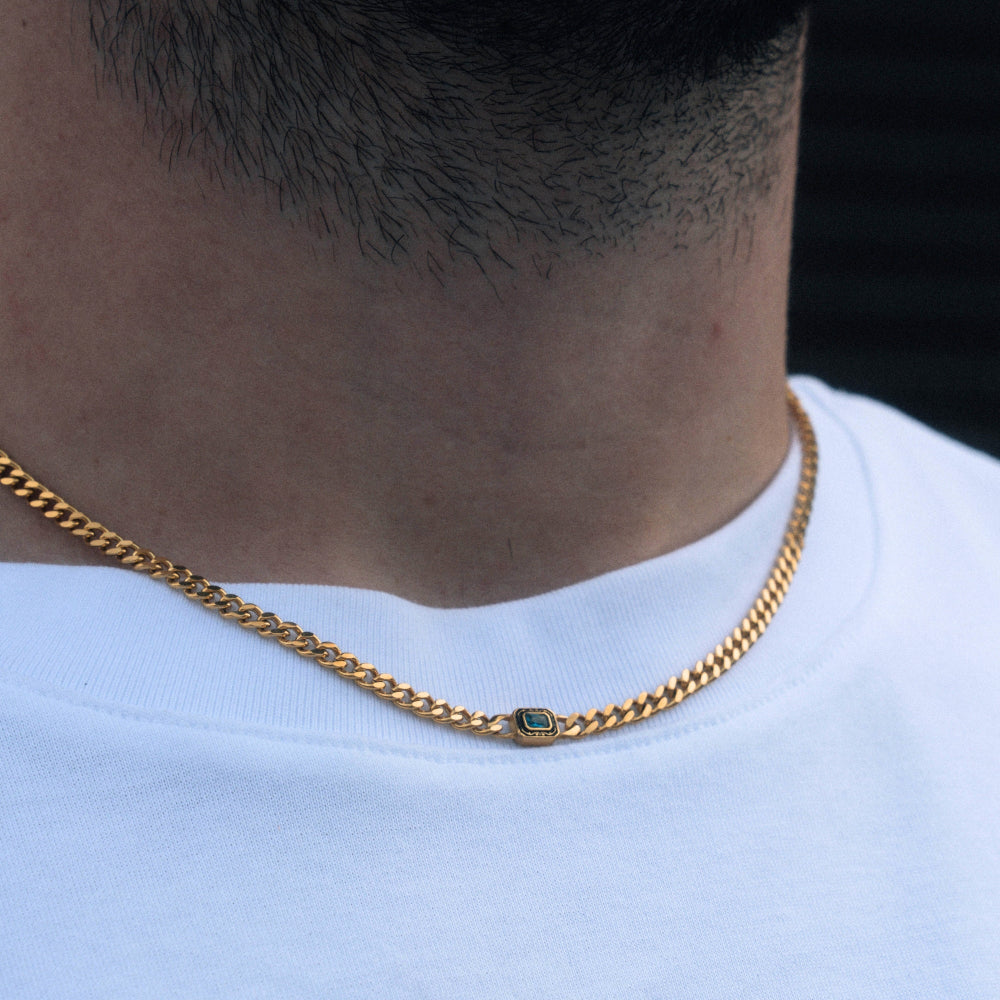 Gold chain necklace with a green gemstone on a person wearing a white shirt.