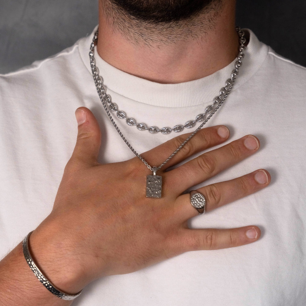Person wearing silver chain necklace, ring, and bracelet on a white shirt.