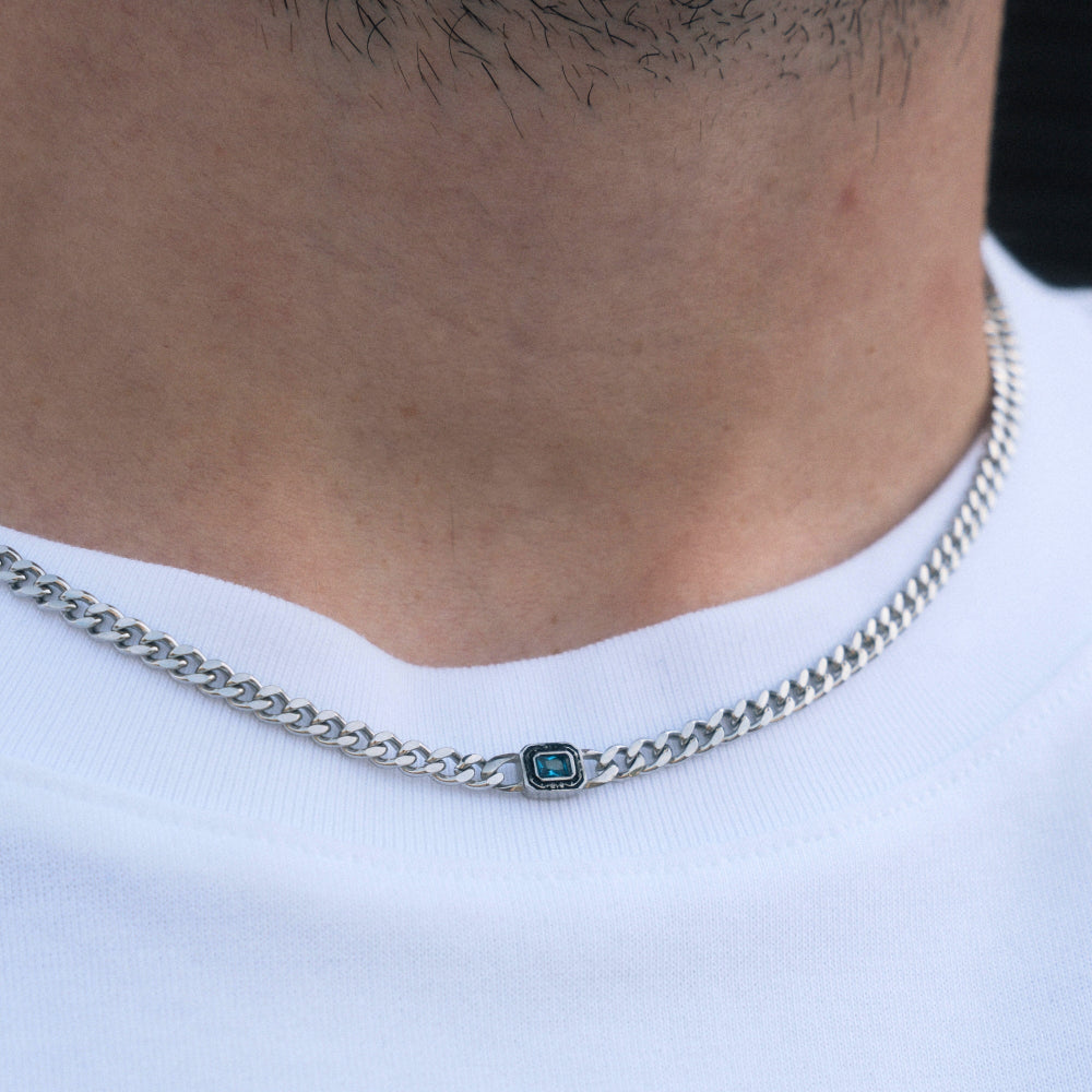 Silver chain necklace with a green gemstone on a white shirt