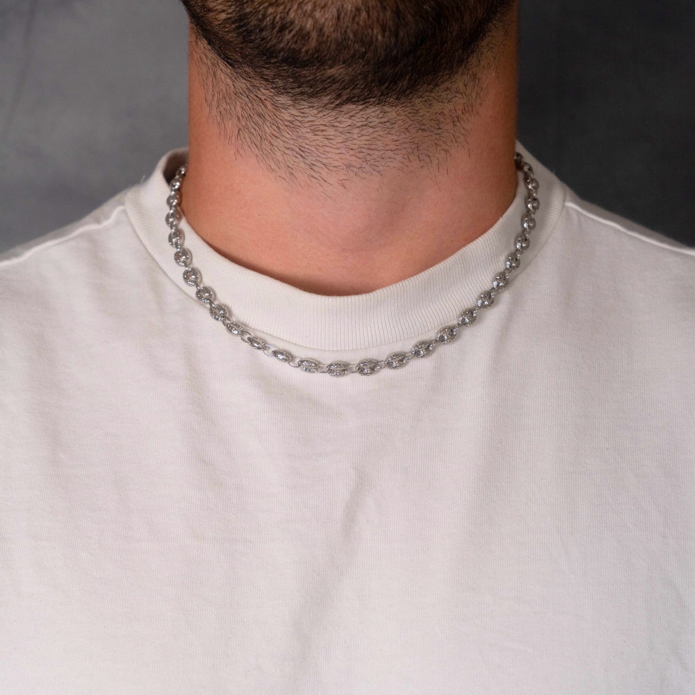 Person wearing a silver chain necklace with a plain background