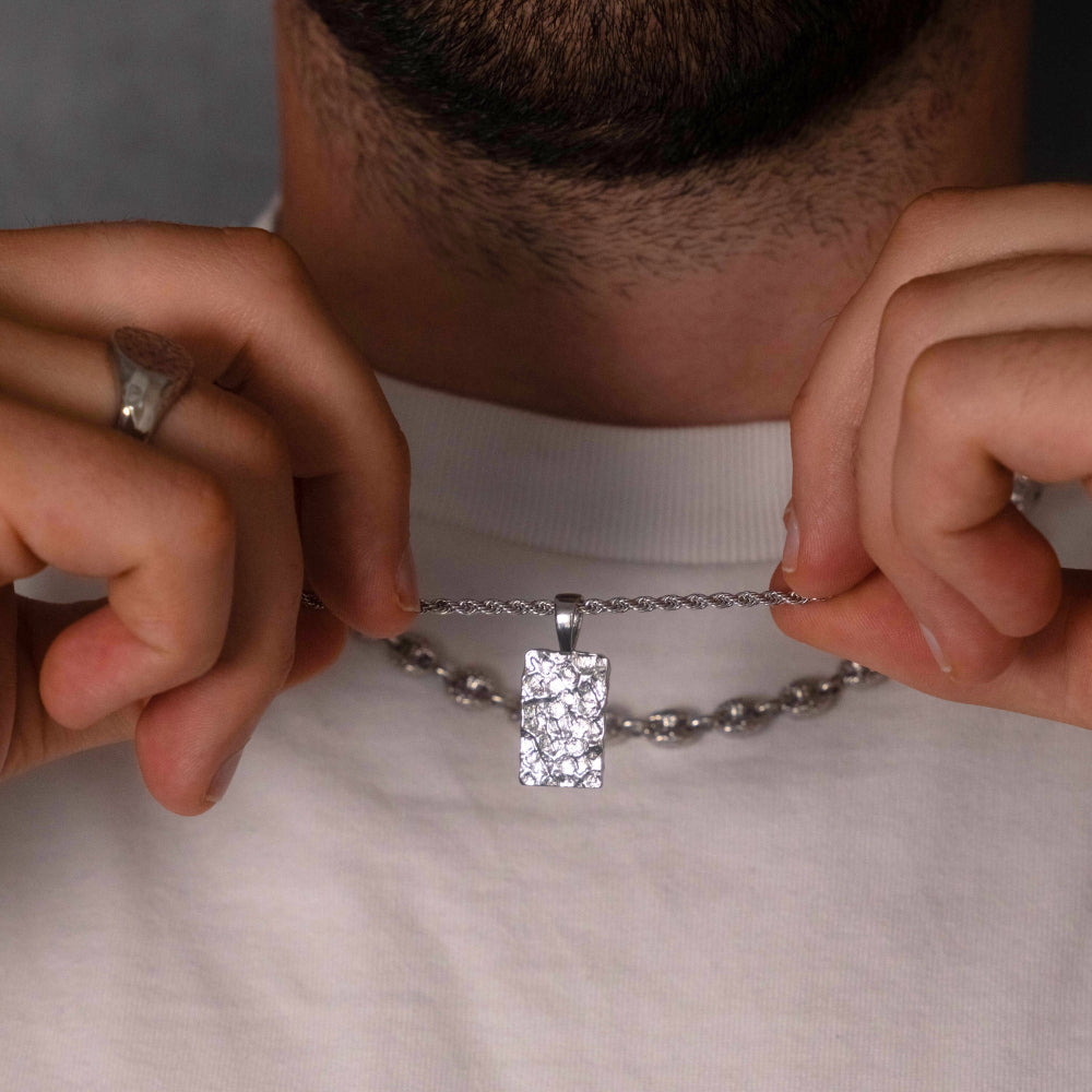 Person holding a silver necklace with a rectangular pendant