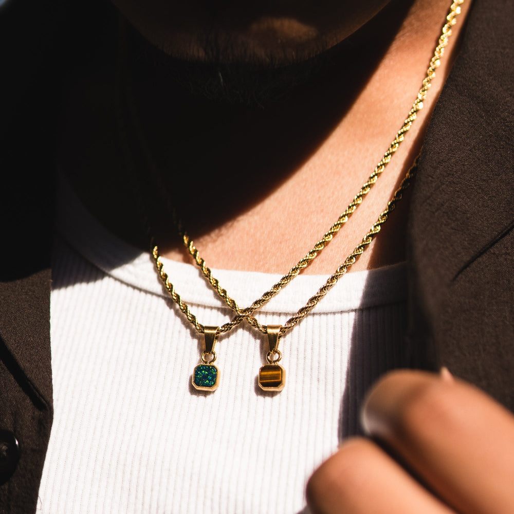 Person wearing a gold necklace with pendant on a plain background