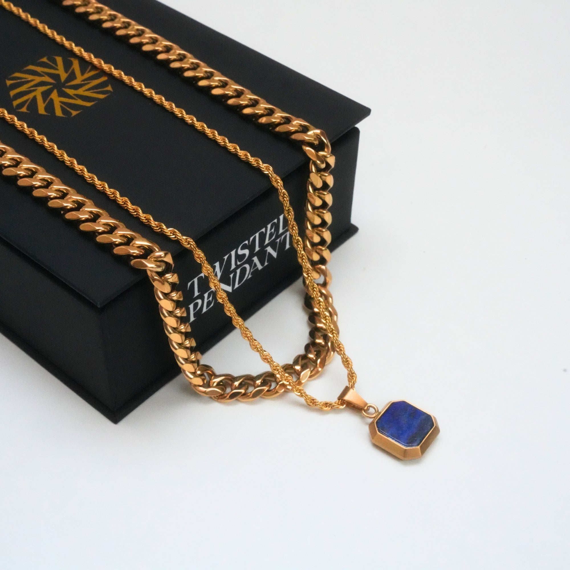 Gold chain necklace with a blue pendant on a black box labeled 'Twisted Pendant'.