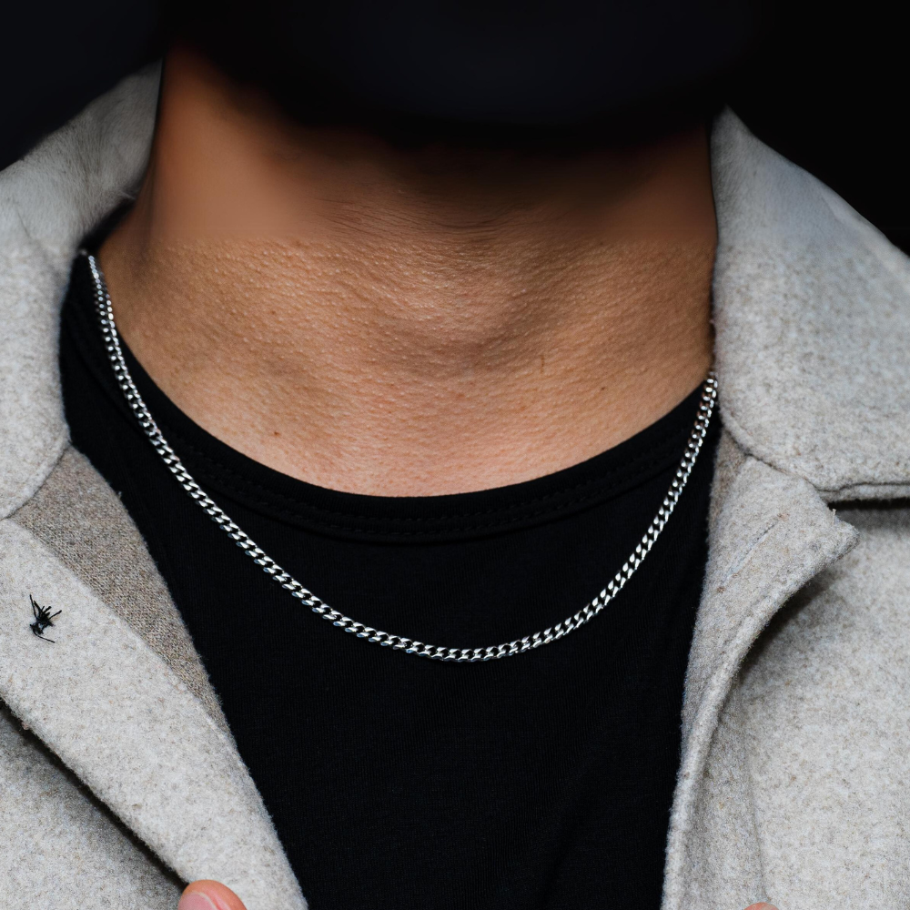 Person wearing a silver chain necklace with a black shirt and gray coat.