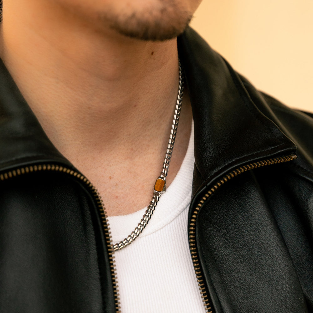 Person wearing a black leather jacket with a chain necklace featuring an orange stone.