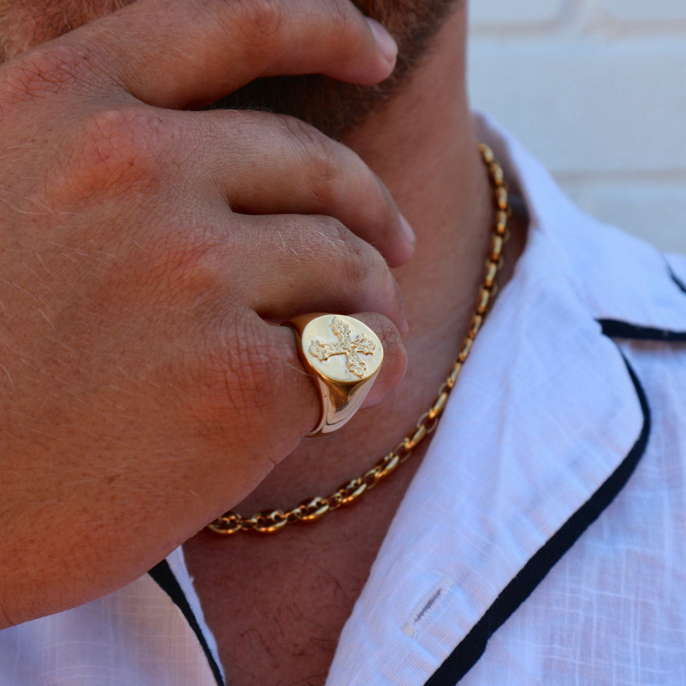 Close-up of a person wearing a gold ring and necklace, with a blurred background.