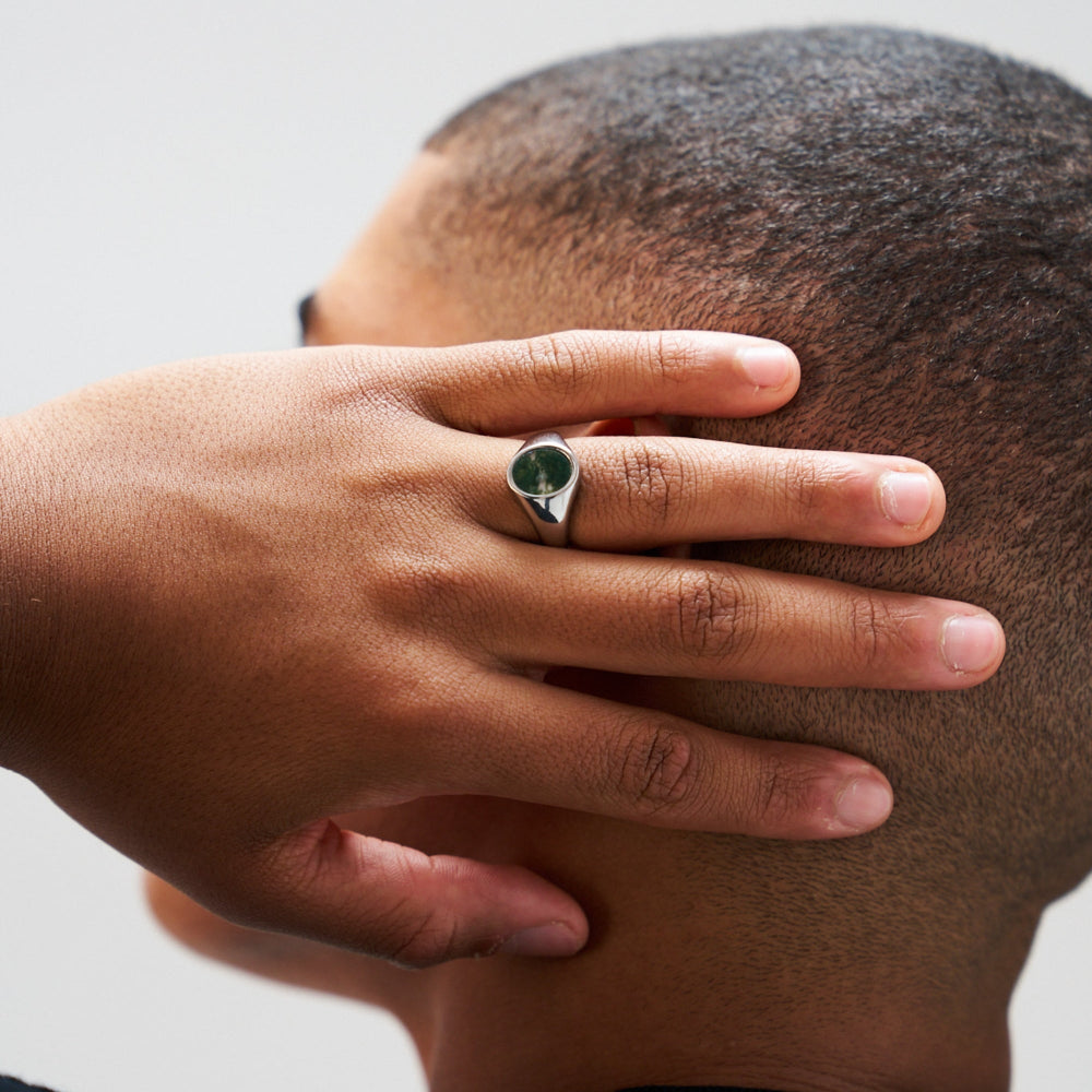 Hand with a ring on a person's finger, holding their head against a neutral background