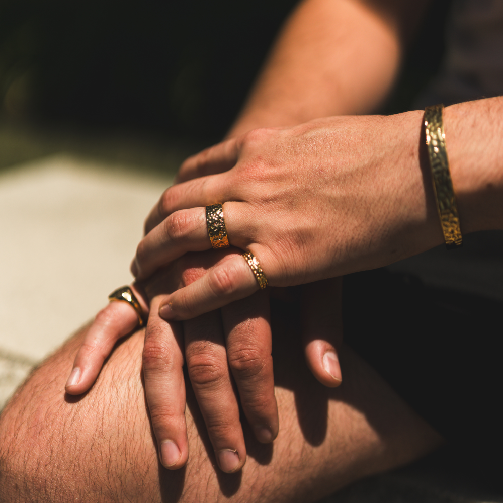 Close-up of two hands holding each other with gold rings and bracelets.