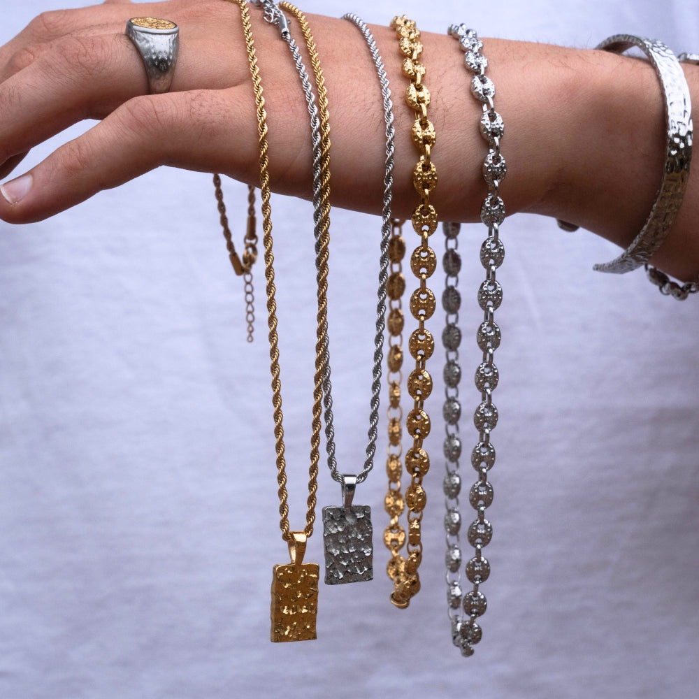 Hand wearing multiple necklaces and bracelets on a plain background