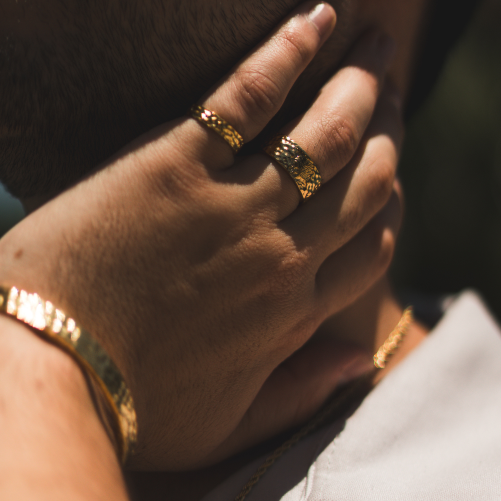 Close-up of a hand wearing gold rings and bracelets against a dark background