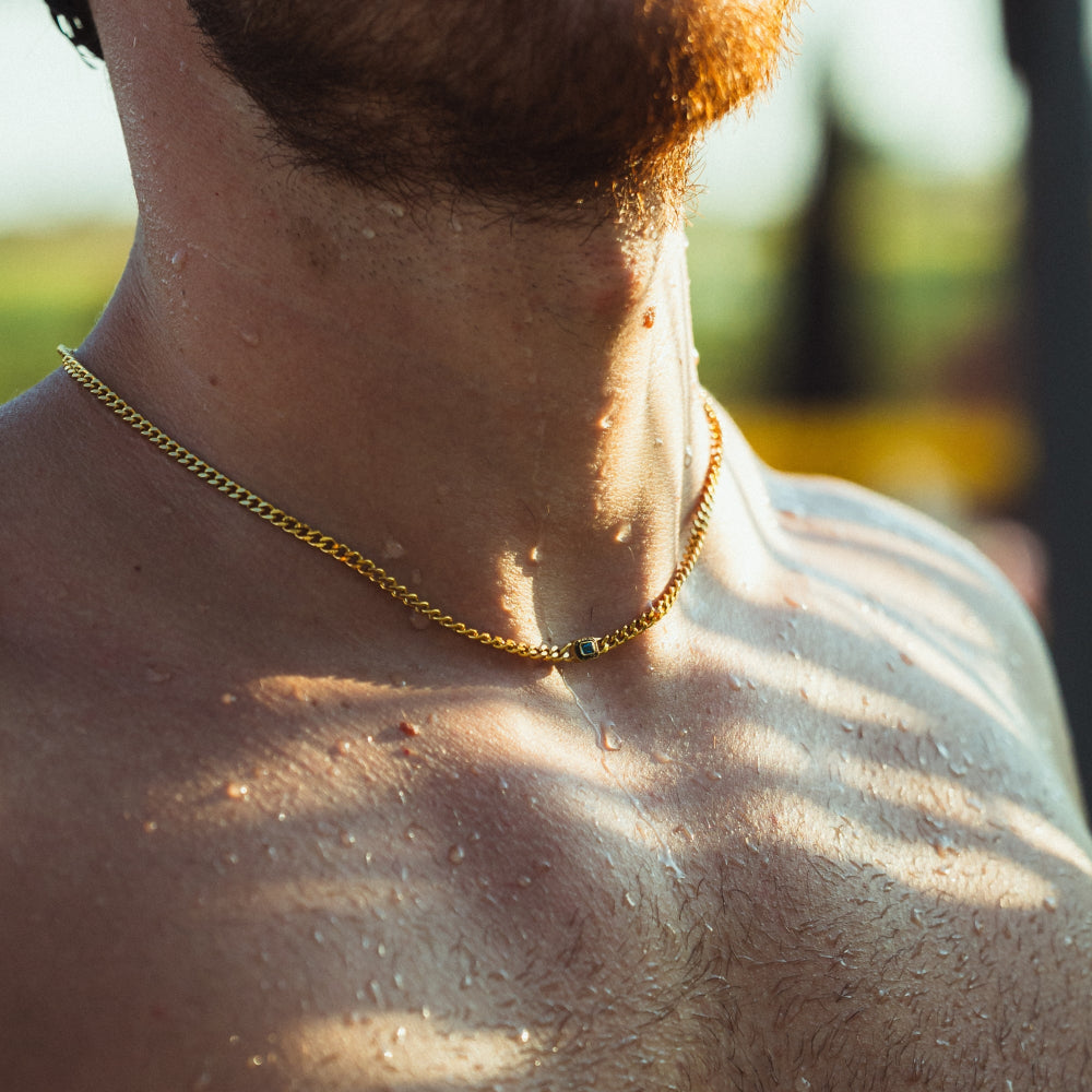 Close-up of a person wearing a gold chain necklace with a blurred outdoor background