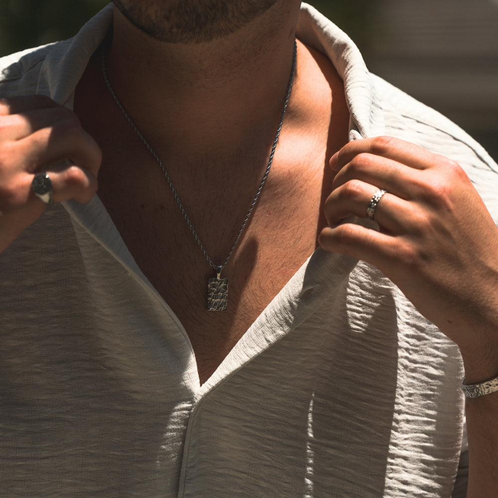 Person wearing a necklace with a pendant, close-up of neck and hands.
