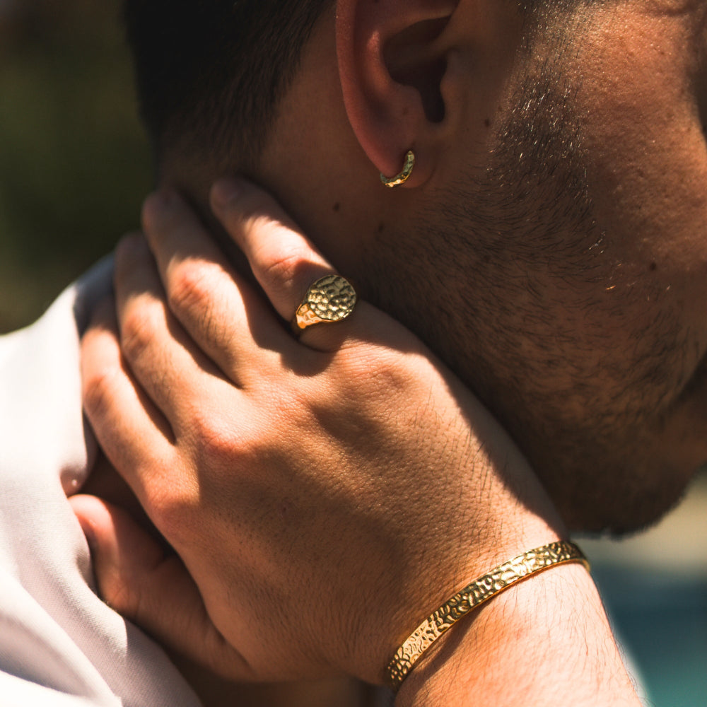 Man wearing gold earrings and a bracelet with a blurred natural background
