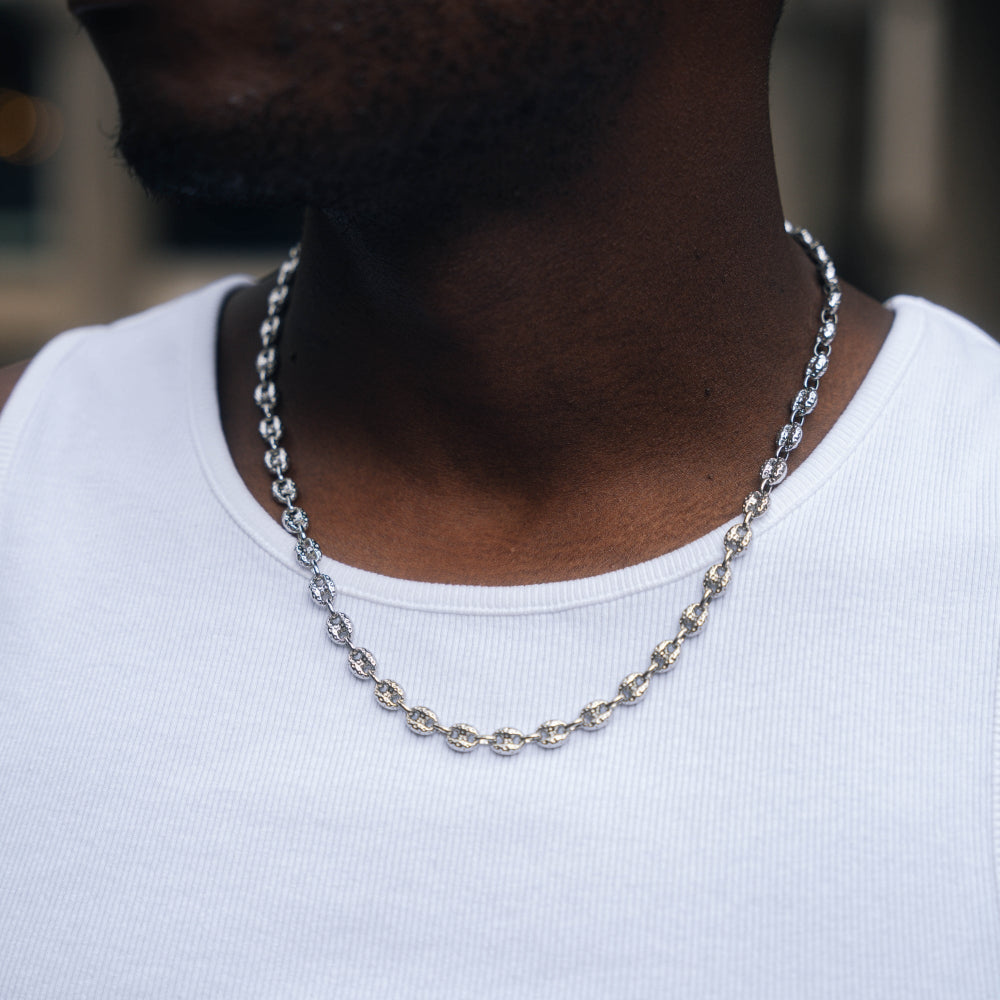 Silver chain necklace on a person wearing a white shirt with a blurred background