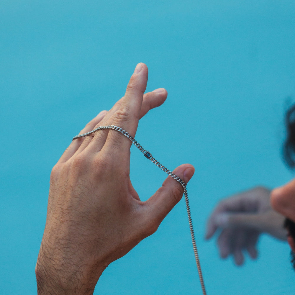 Hand holding a chain against a blue background