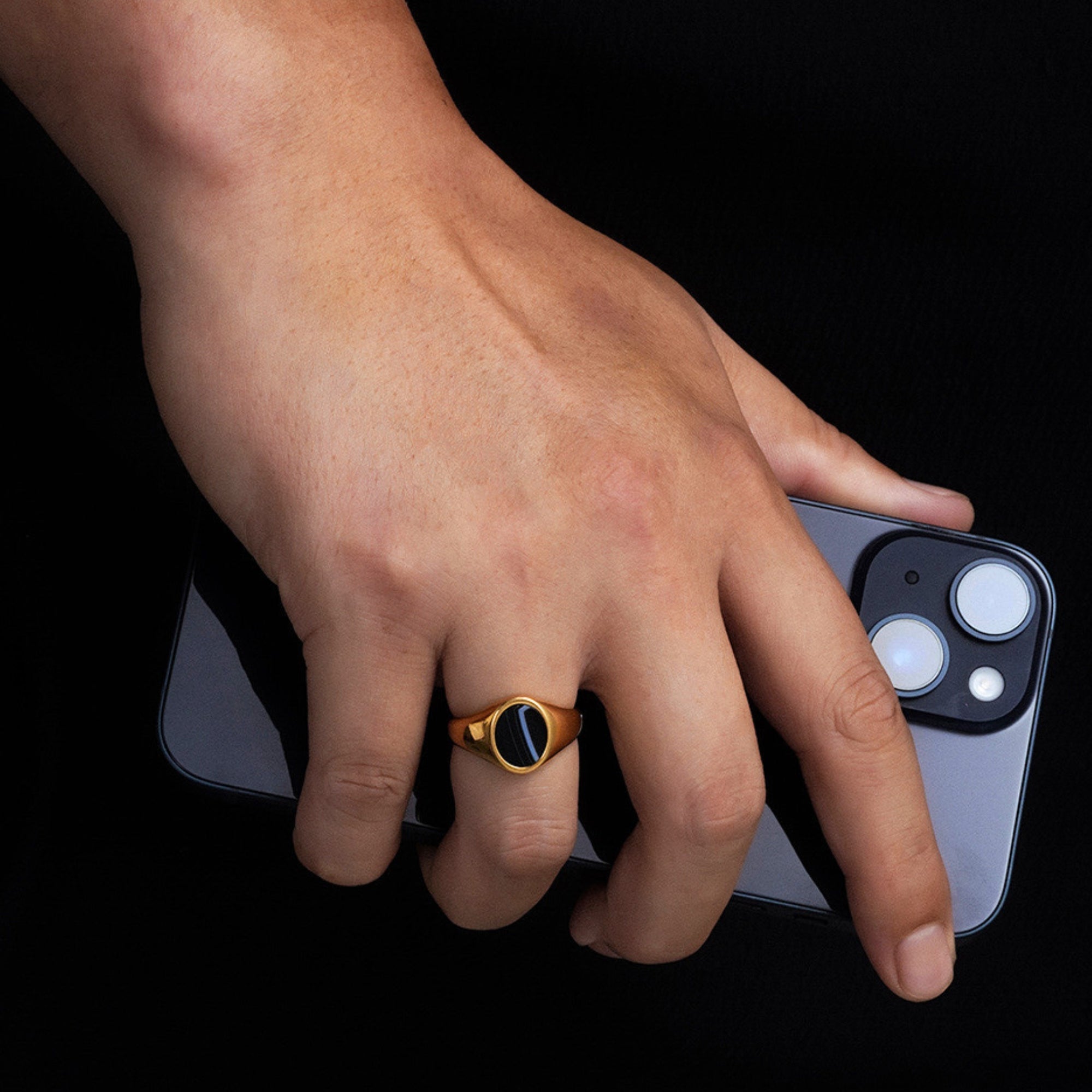 Hand holding a smartphone with a gold ring on a black background