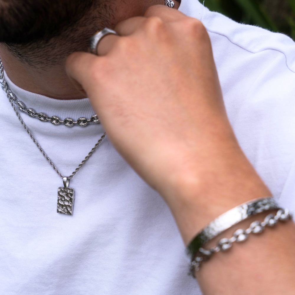 Person wearing multiple silver necklaces and bracelets on a white shirt background