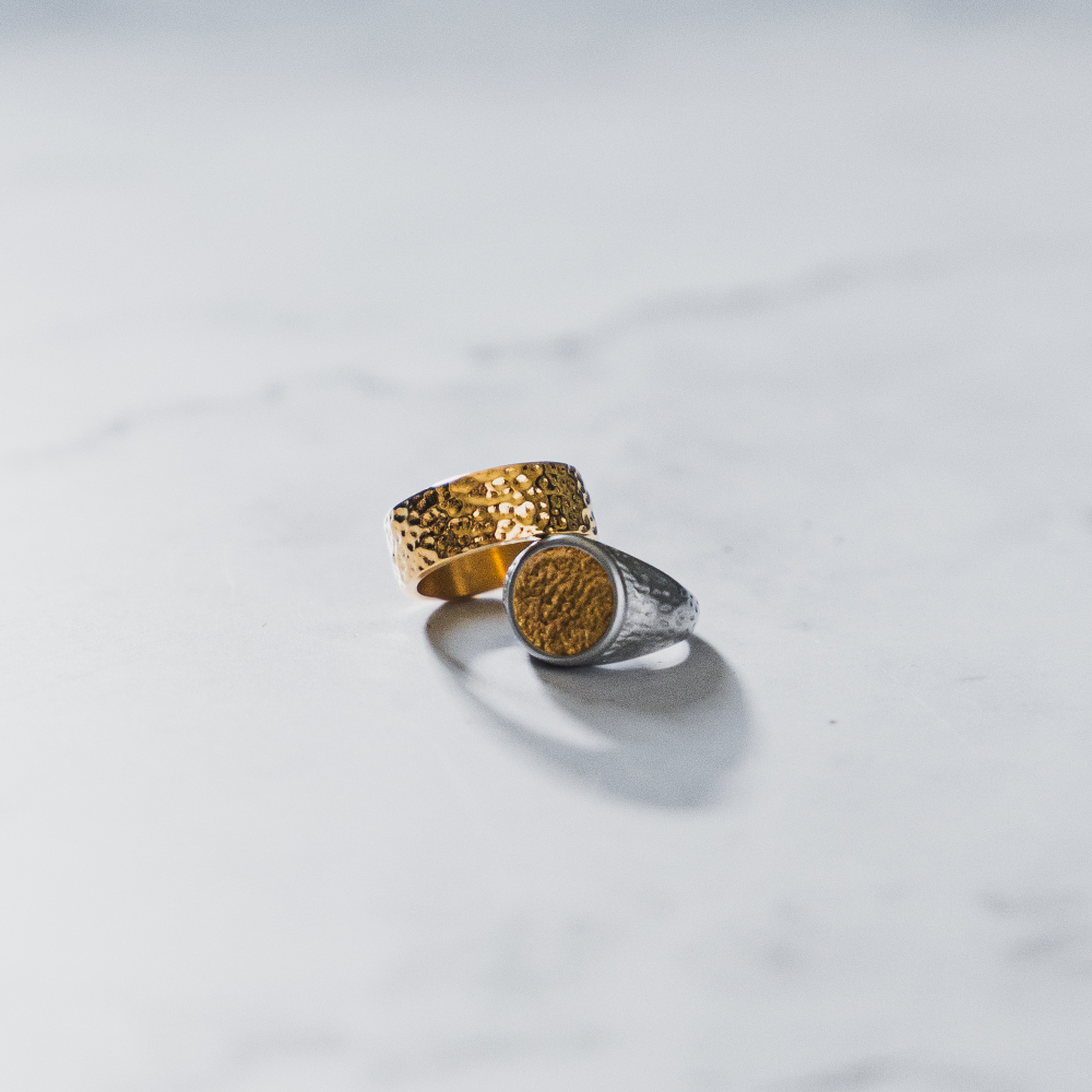 Two textured rings, one gold and one silver, on a light gray background