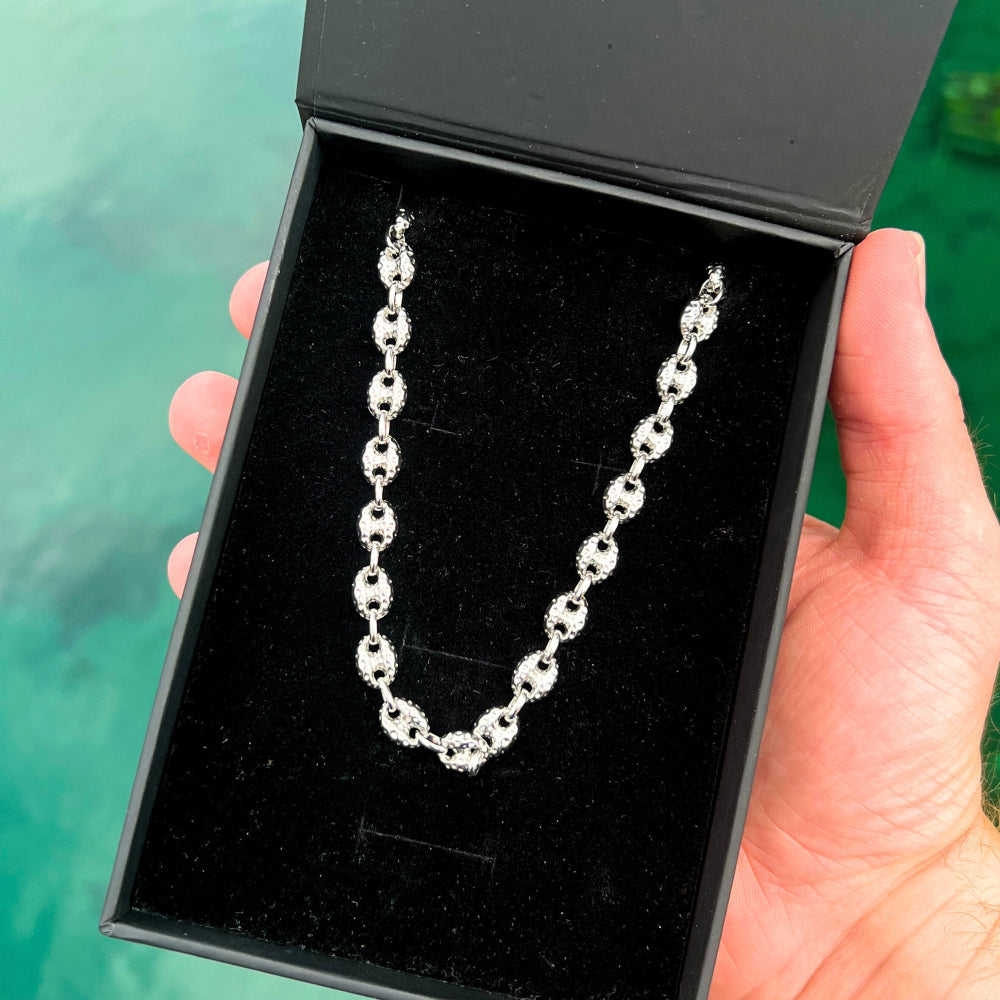Silver bracelet in a black jewelry box held by a hand against a green background