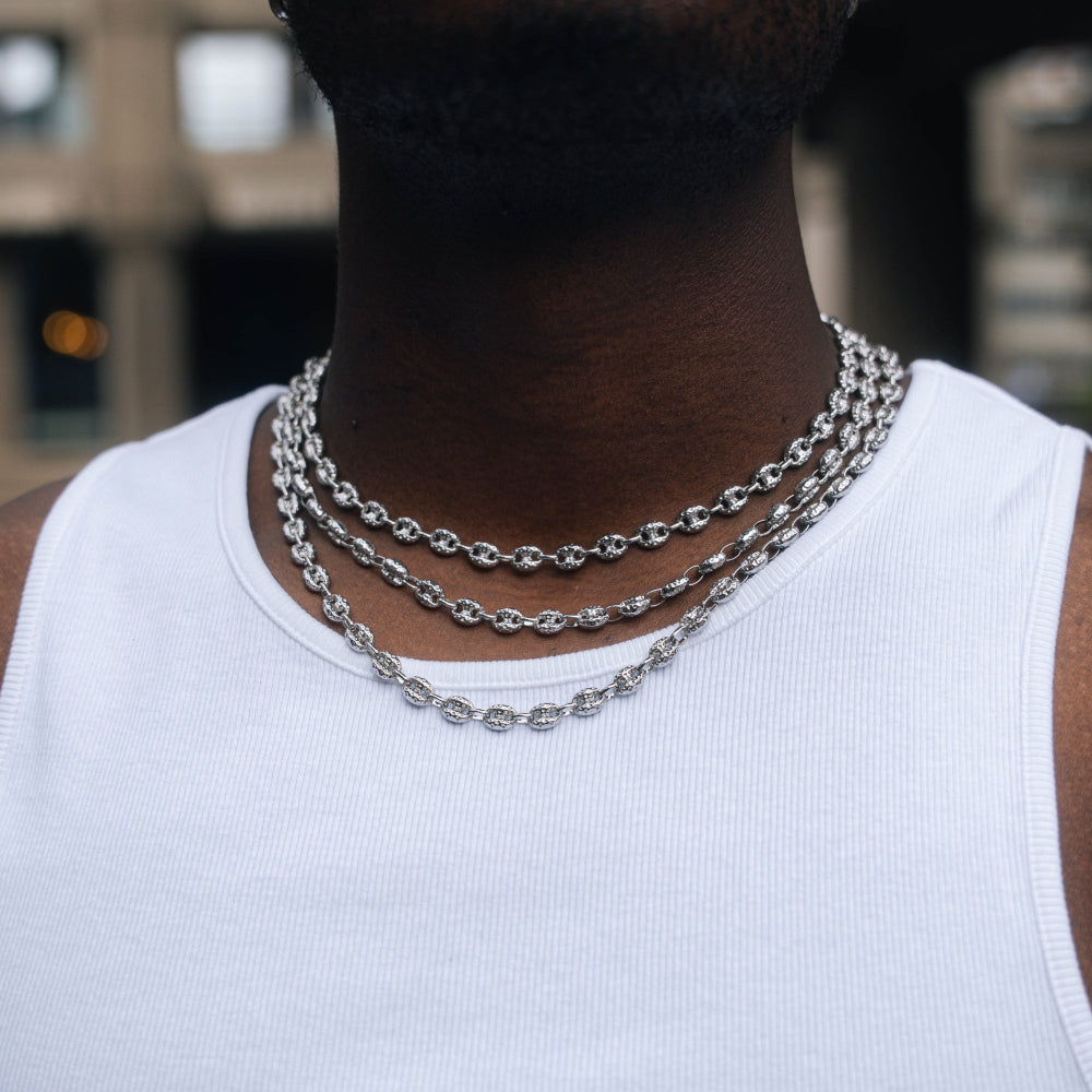 Person wearing two silver chain necklaces on a blurred background