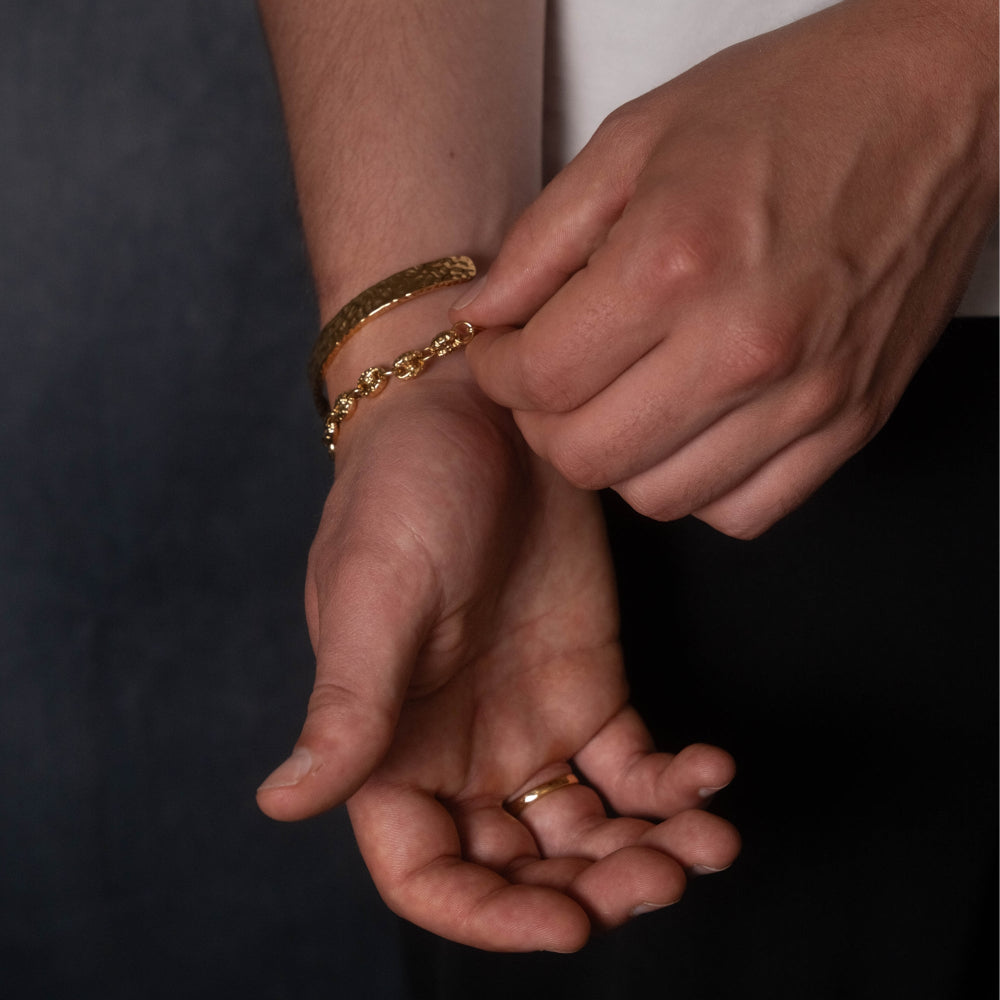 Close-up of hands wearing gold bracelets and a ring on a dark background
