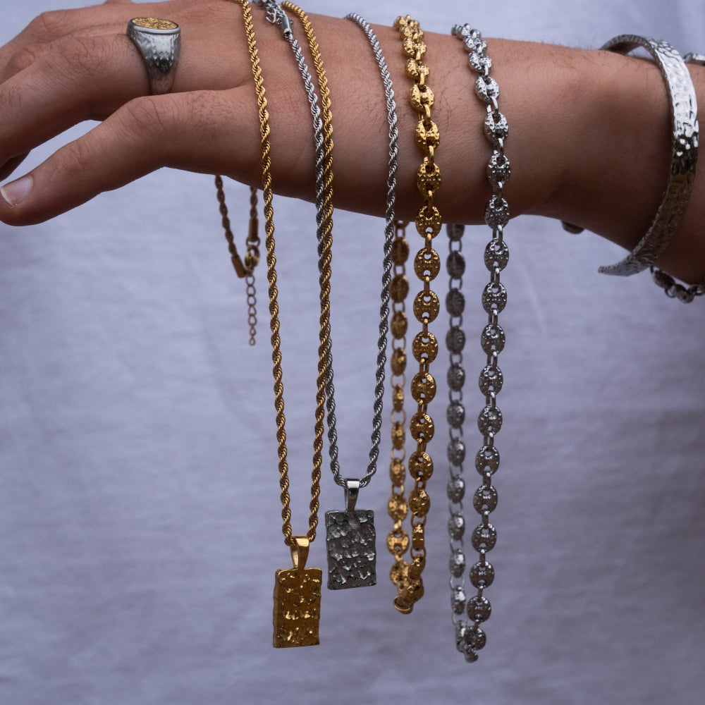 Hand wearing multiple gold, silver, and bronze necklaces on a gray background