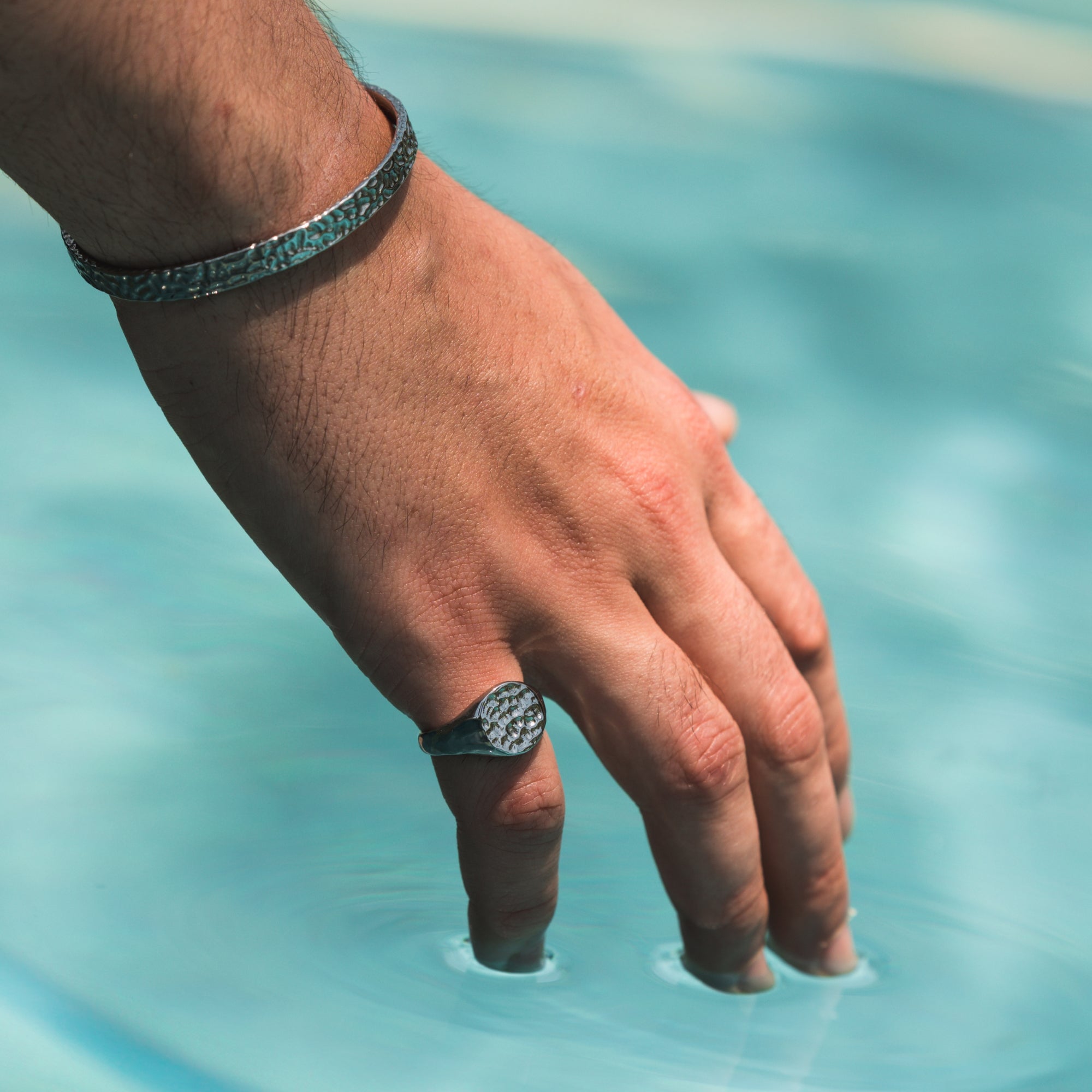 Hand with a ring touching clear blue water