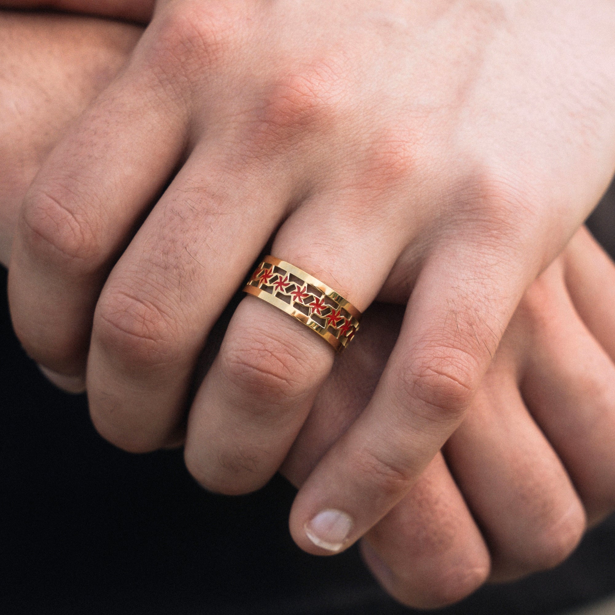 Gold ring with red accents on a finger against a blurred background