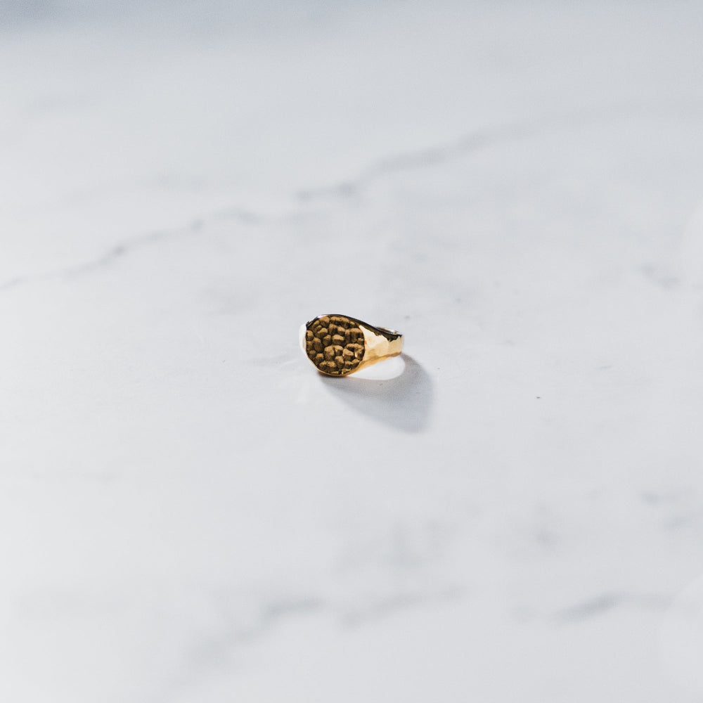 Gold ring with textured design on a light gray marble surface