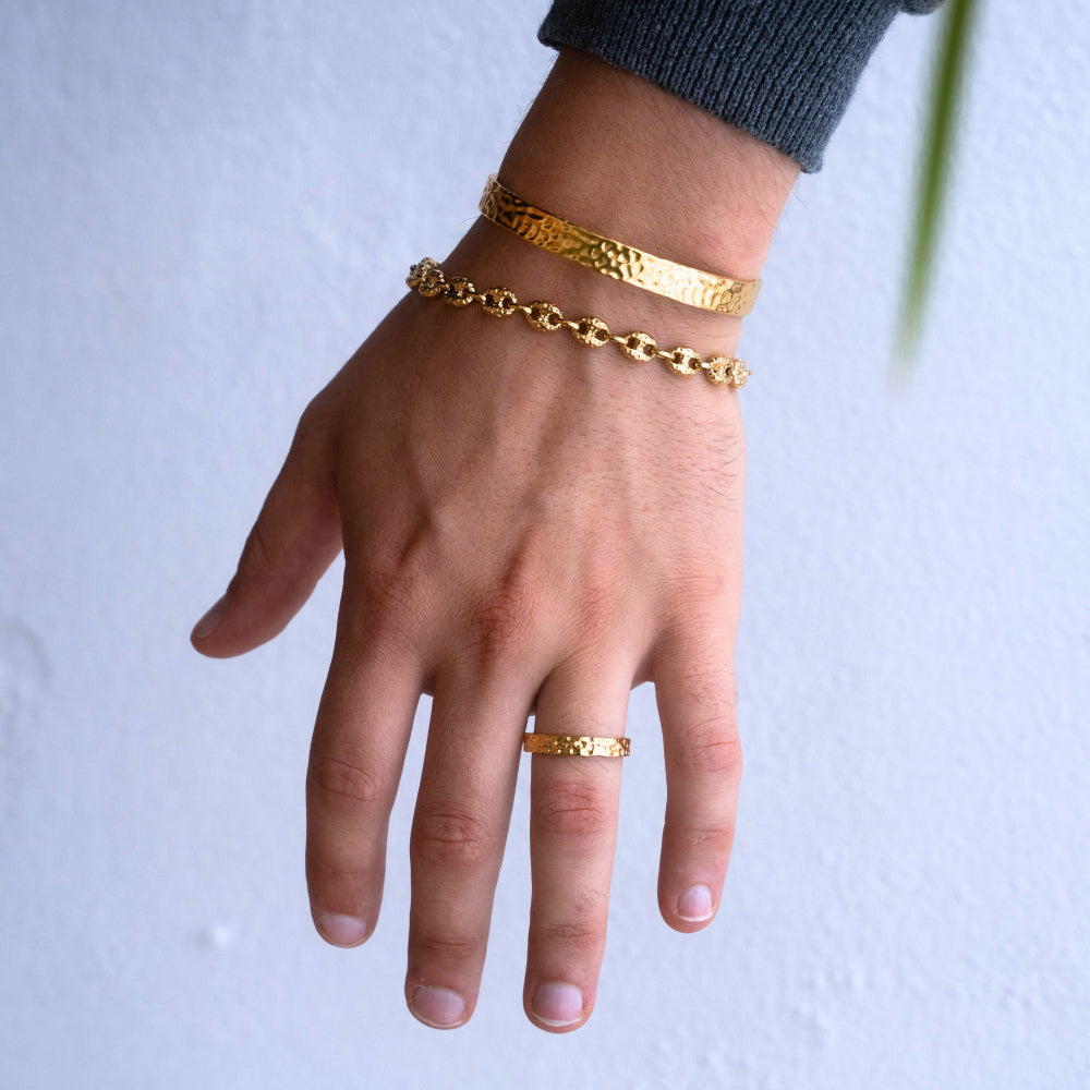 Hand wearing gold bracelets and a ring on a white background