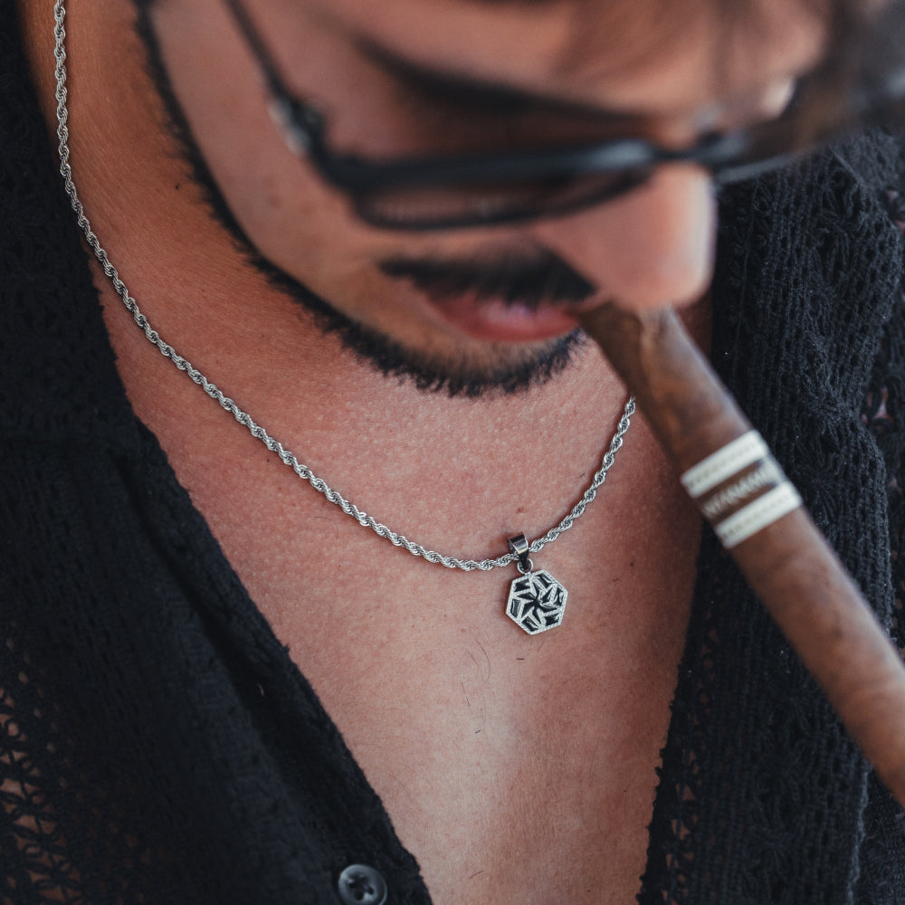 Person wearing a silver necklace with a pendant, holding a cigar.