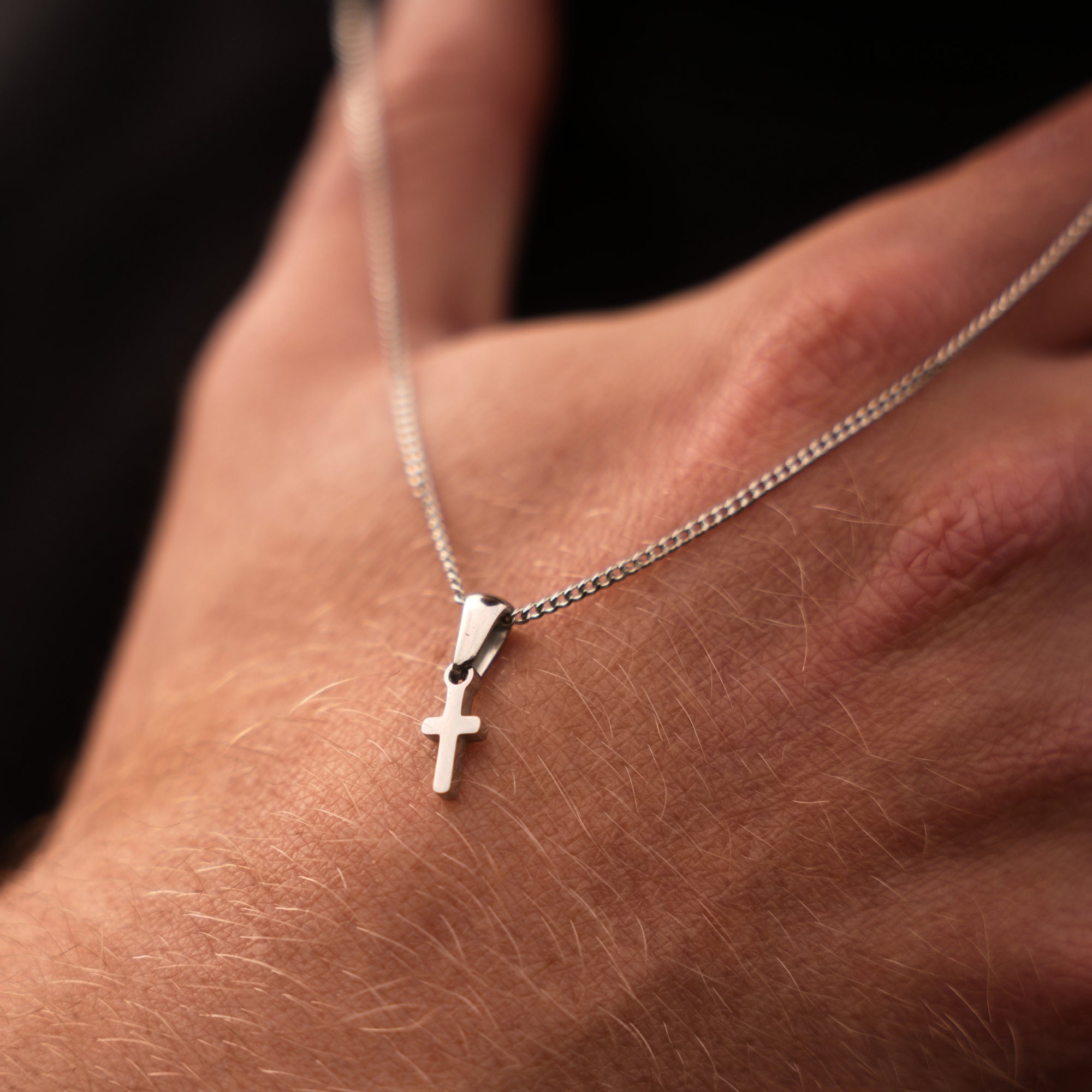 Silver cross necklace on a hand against a dark background