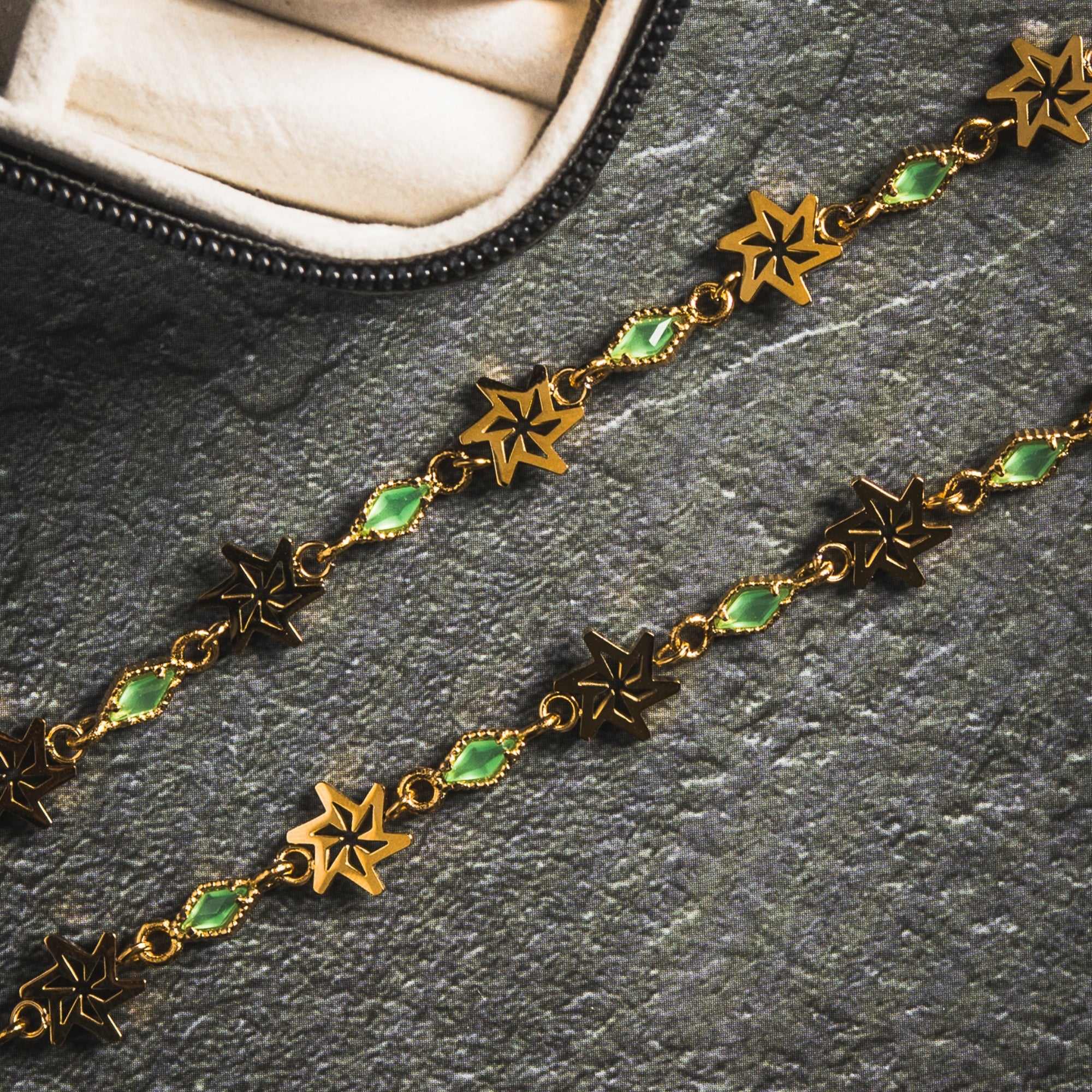 Gold chain necklace with star and green gemstone pendants on a dark surface