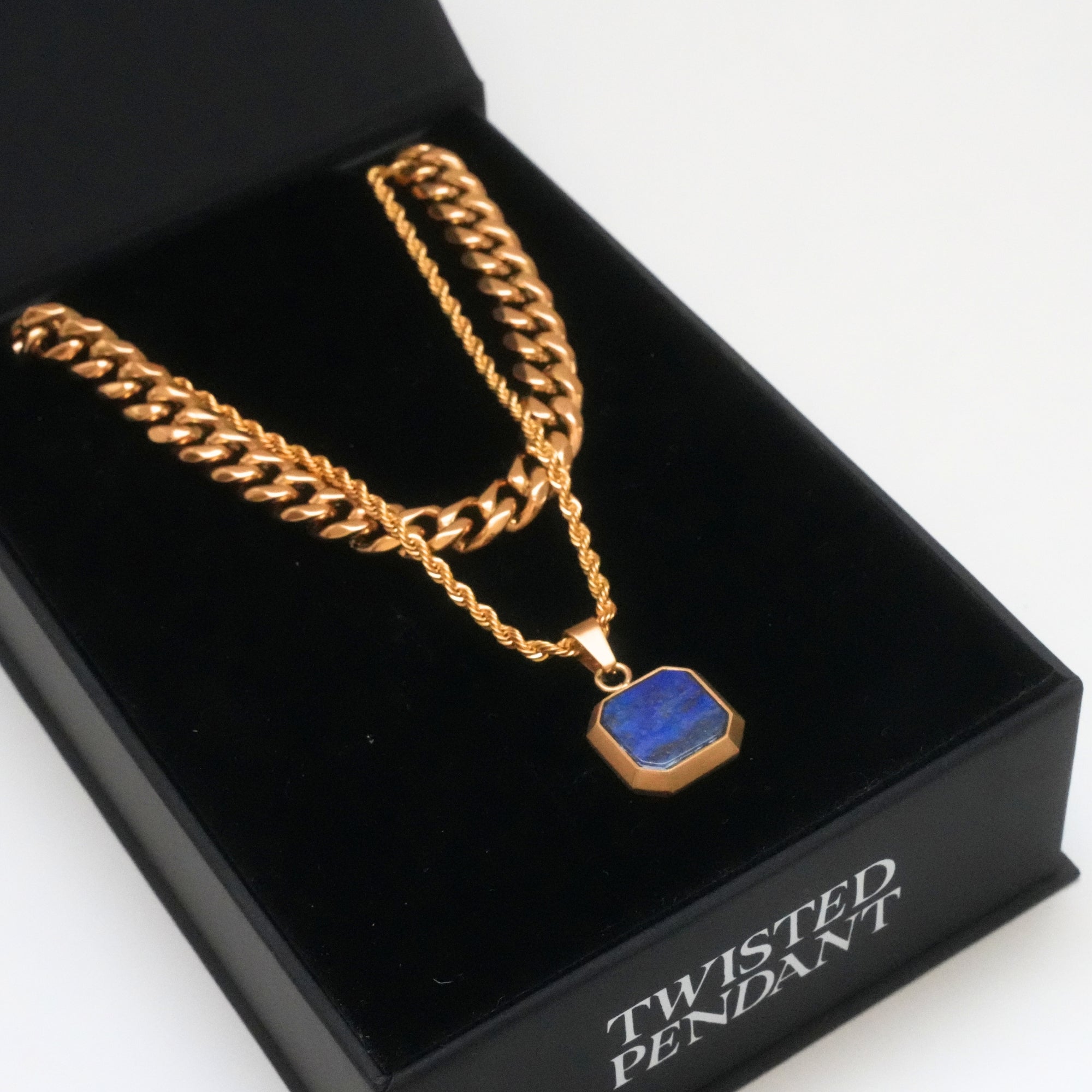 Gold chain necklace with a blue pendant on a black box labeled 'Twisted Pendant'.