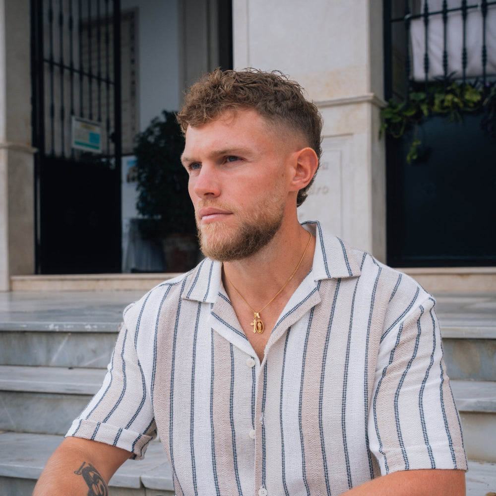 Man with a beard wearing a striped shirt sitting outdoors.