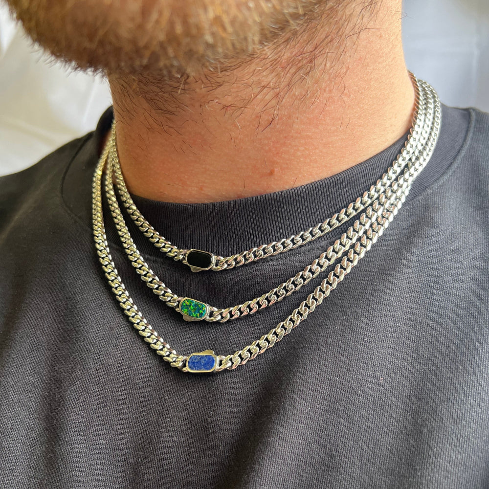 Close-up of a person wearing two gold chains with gemstones on a plain background
