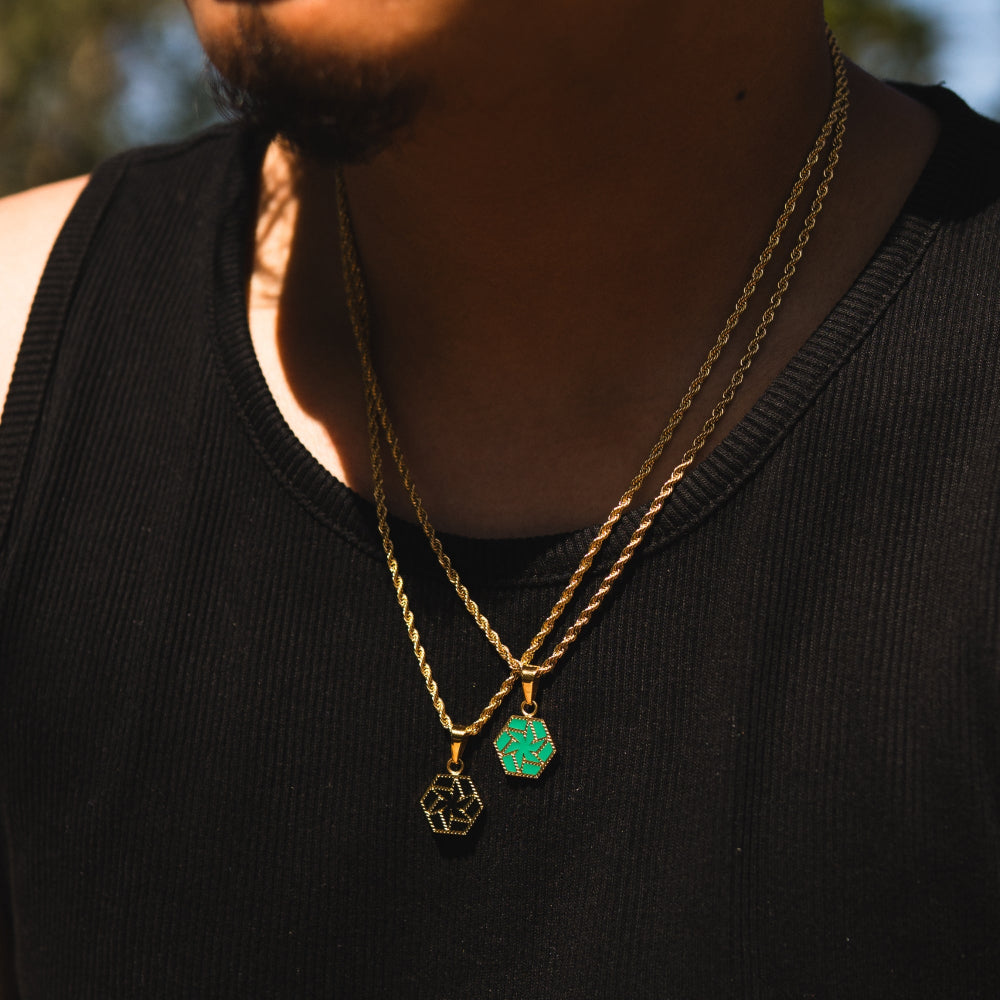 Person wearing two gold necklaces with green pendants against a blurred natural background