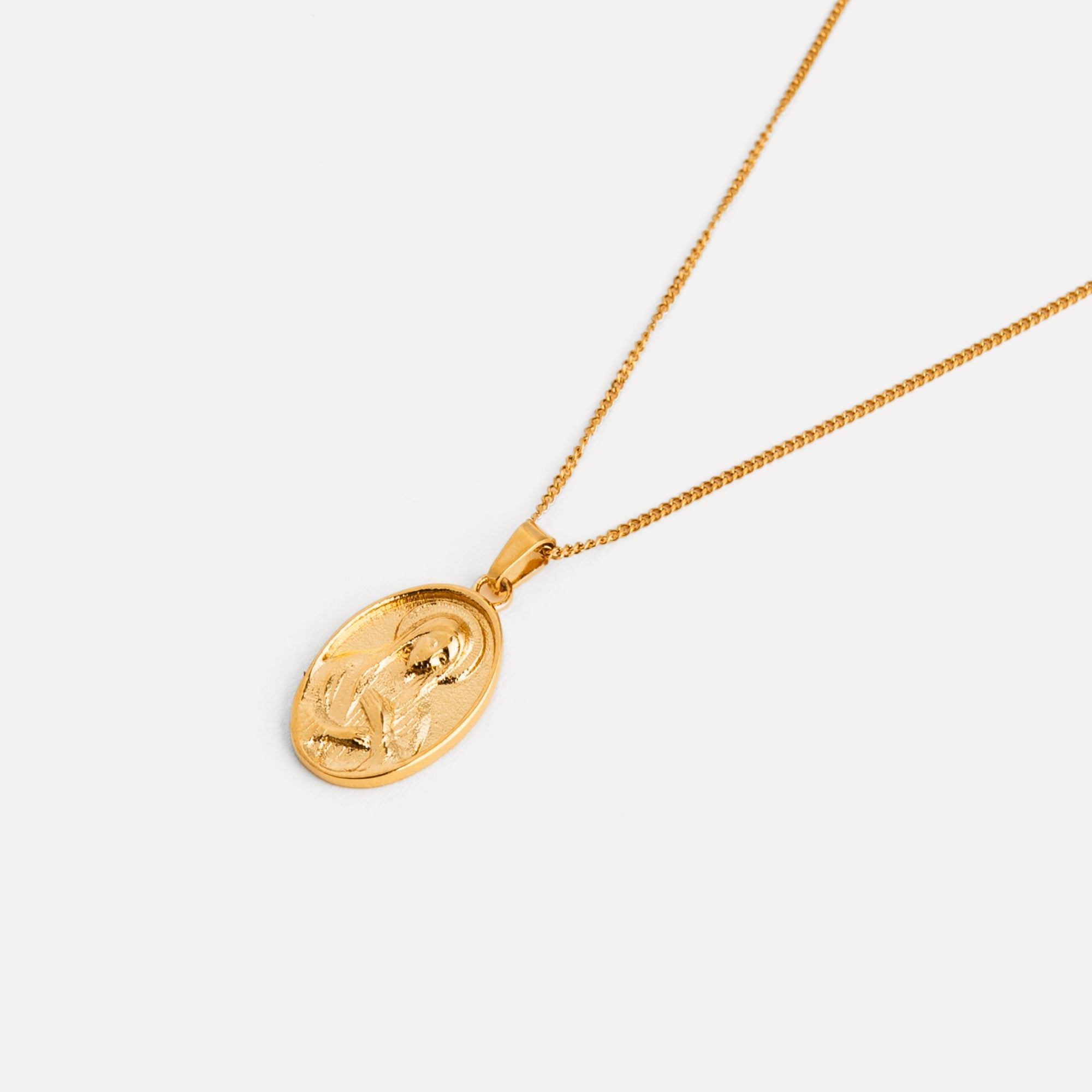 Gold necklace with a round pendant on a light gray background