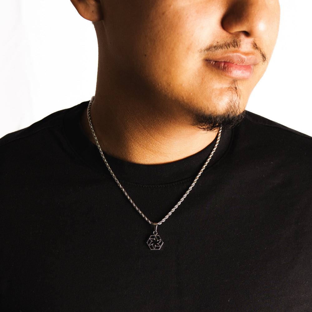 Person wearing a black shirt with a necklace featuring a small pendant.