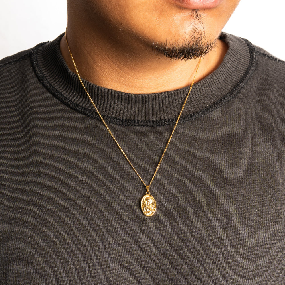 Gold necklace with a pendant worn by a person in a black sweater.