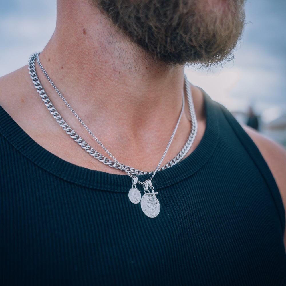 Close-up of a person wearing two silver necklaces with pendants.