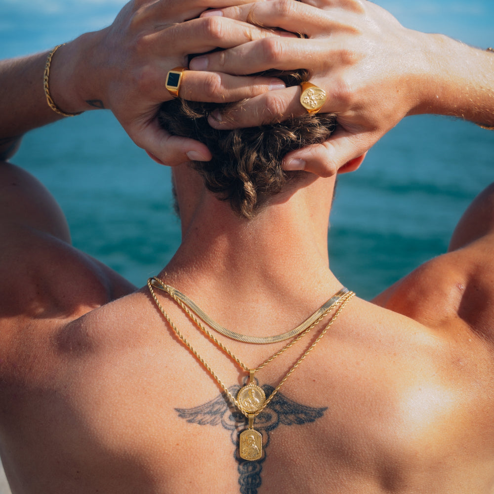 Person with gold jewelry and tattoos against a blue ocean background