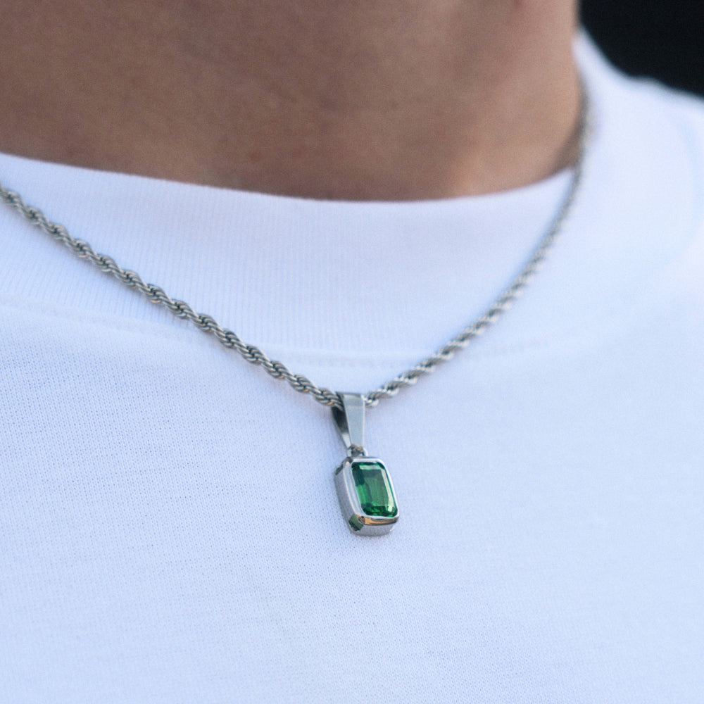 Green gemstone pendant on a silver chain against a white shirt background