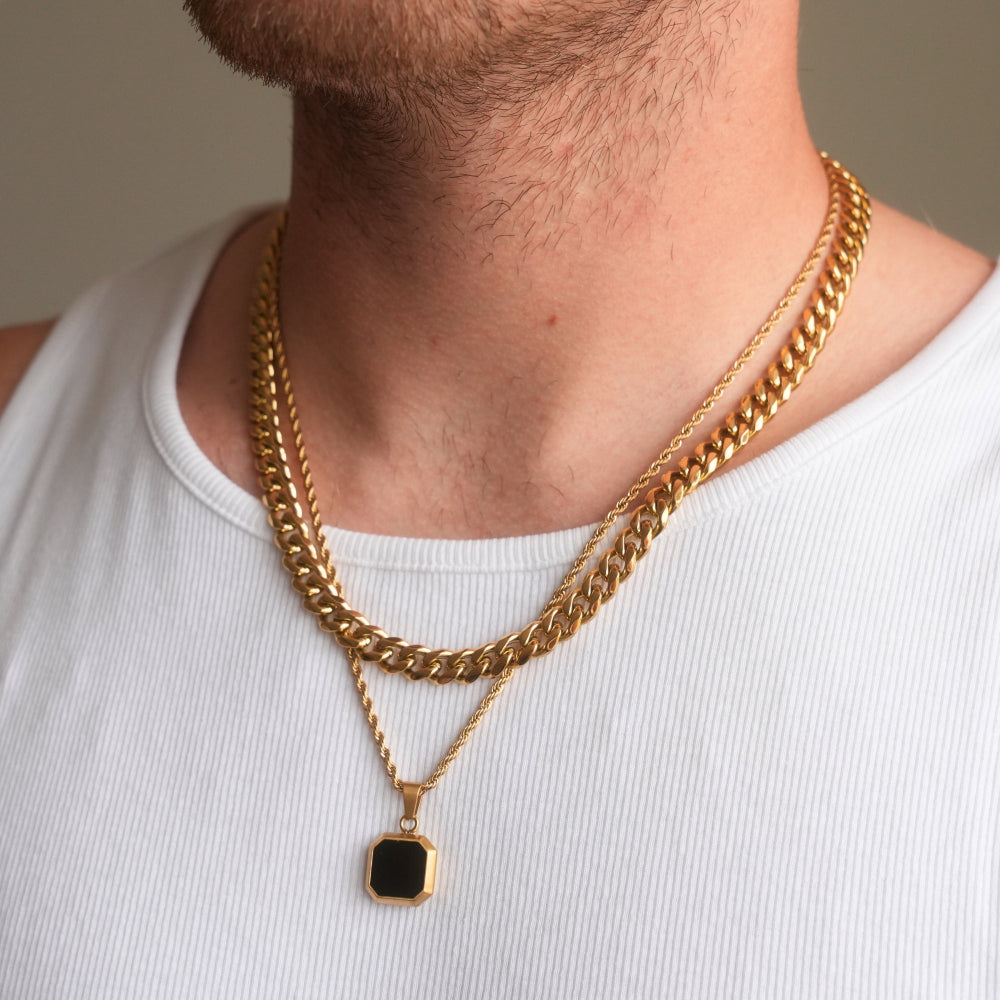 Gold chain necklace with a pendant on a person wearing a white tank top.