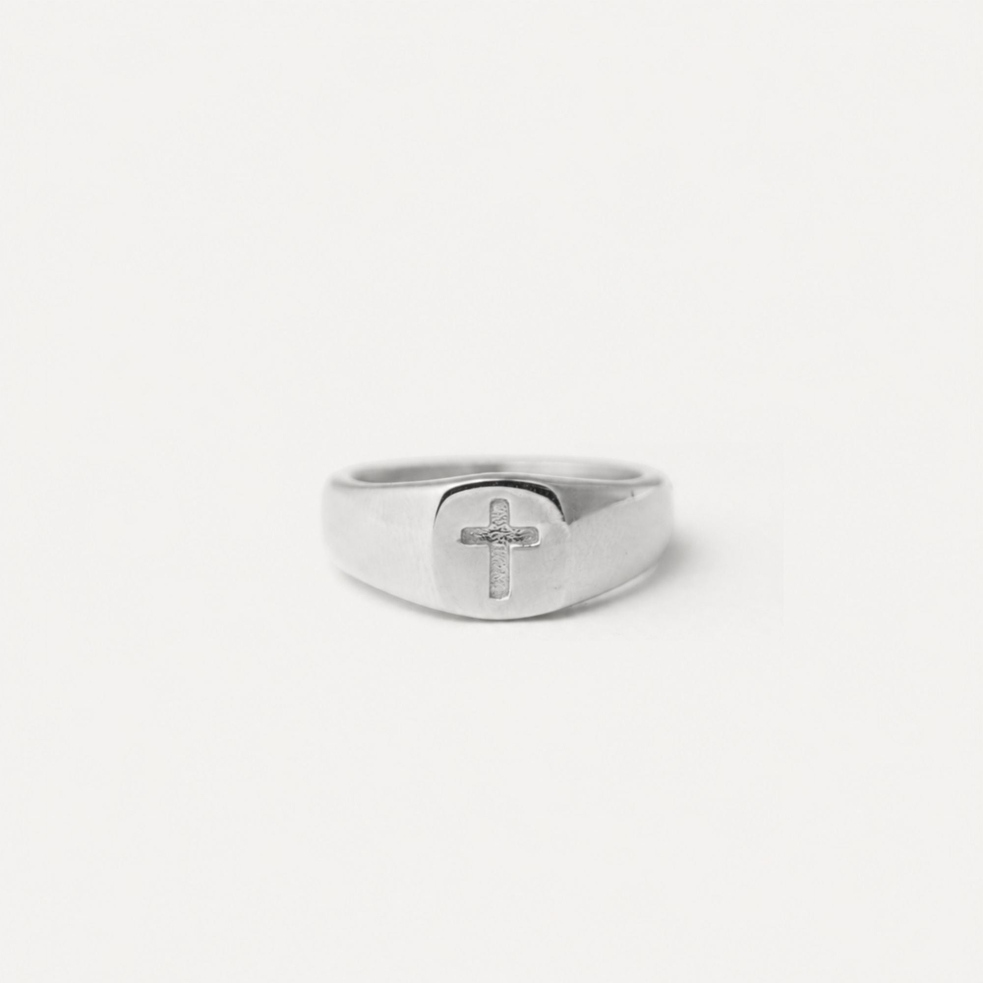 A silver signet ring with a polished cross emblem on the face, photographed against a seamless white background.